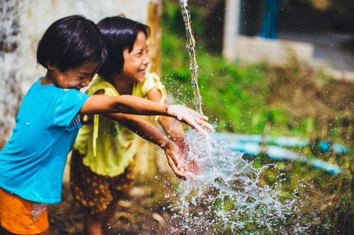 Two children playing with water in a yard.