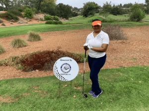 A woman holding onto her golf club while standing next to a sign.