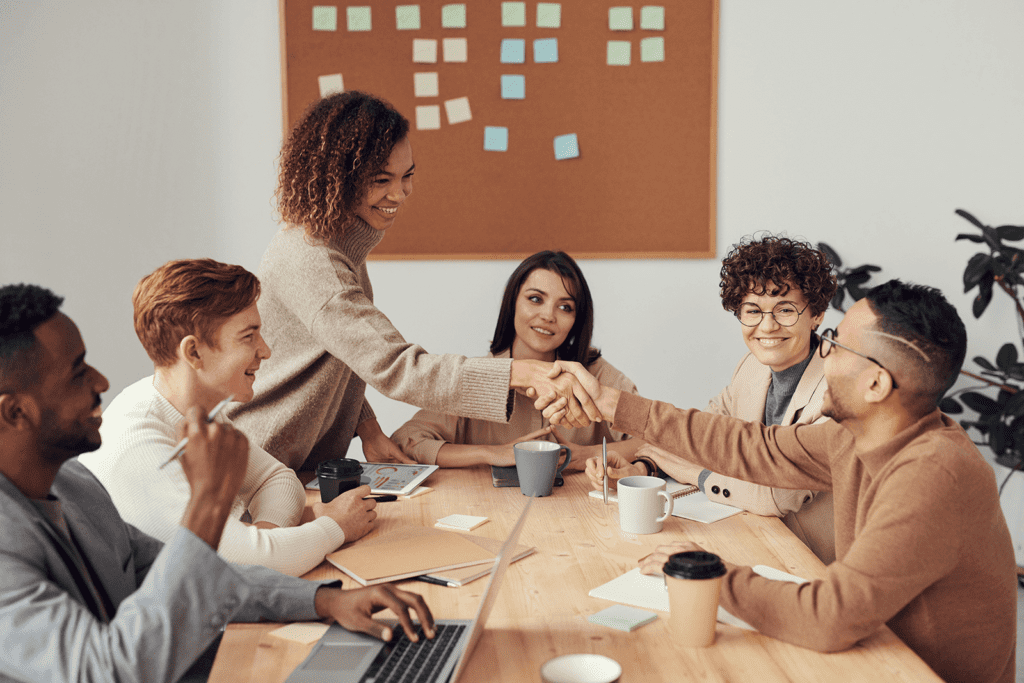 A group of people sitting around a table shaking hands.